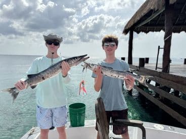 Two young anglers proudly displaying their Barracuda catch at a dockside location, showcasing a successful fishing trip.
