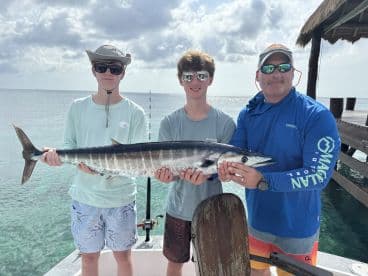 Two young anglers and an adult proudly displaying a large Mahi Mahi on a fishing charter in clear waters.