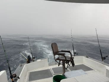 View from the helm of a fishing boat navigating through rough waters, showcasing the fishing rods and seating area.