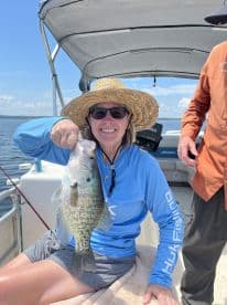 An adult angler proudly displaying a Crappie while fishing on a sunny day, showcasing a relaxing day on the water.