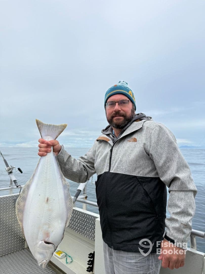 An angler proudly displaying a large Halibut on a fishing charter in open waters, showcasing a successful catch.