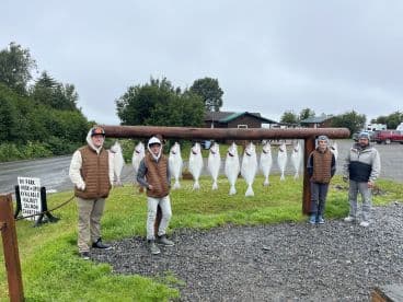 Group of anglers proudly displaying their catch of Halibut on a catch board after a successful fishing trip.