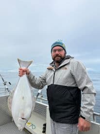 An angler proudly displaying a large Halibut on a fishing charter in open waters, showcasing a successful catch.