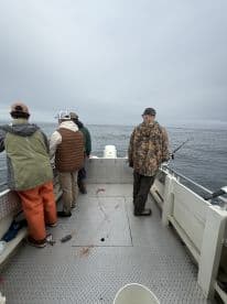 Group of anglers engaged in fishing on a charter boat, with a calm ocean backdrop and cloudy skies.