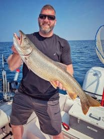 An angler proudly displaying a large Lake Trout while fishing on a sunny day, showcasing the excitement of a successful catch.