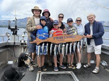 A family group proudly displaying their catch of trout on a fishing charter at Lake Tahoe, with a scenic backdrop of mountains.
