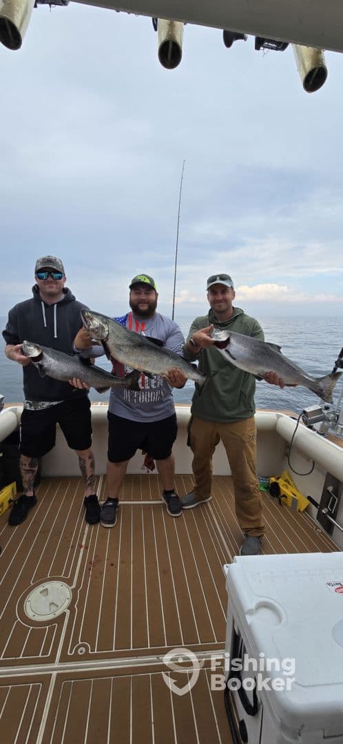Three anglers proudly displaying their catch of large Salmon aboard a fishing charter in open waters.