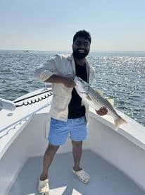 Angler proudly displaying a striped bass while aboard a fishing boat, enjoying a sunny day on the water.