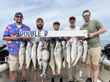 A group of anglers proudly displaying their catch of multiple Lake Ontario salmon while holding a sign with contact information for the charter.