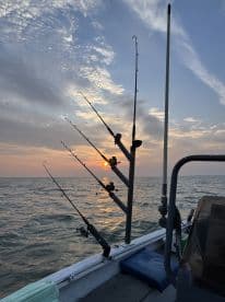 A serene view from the interior of a fishing boat at sunset, showcasing multiple fishing rods set up for a day of deep-sea fishing.
