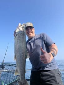 An angler proudly displaying a large Lake Trout while fishing on a sunny day, showcasing the excitement of a successful catch.