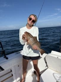 Angler proudly displaying a large Grouper while fishing on a boat in open waters.