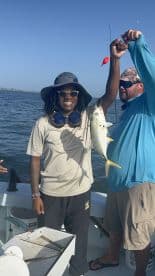A proud angler holding a Yellowtail Snapper while fishing on a boat, showcasing a successful catch during a sunny day on the water.
