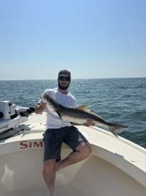 Angler proudly displaying a large fish while sitting on the boat, enjoying a sunny day on the water.