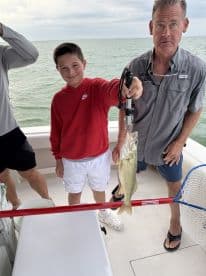 A young angler proudly displaying a Walleye on a fishing charter, with the boat's interior visible in the background.