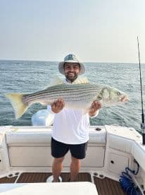 Angler proudly displaying a large Striped Bass while aboard a fishing boat, showcasing a successful day on the water.