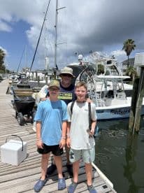 A group of young anglers posing on the dock next to a fishing boat, showcasing a fun day out on the water.