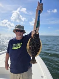 Angler proudly displaying a Flounder while fishing on a boat, showcasing a sunny day on the water.