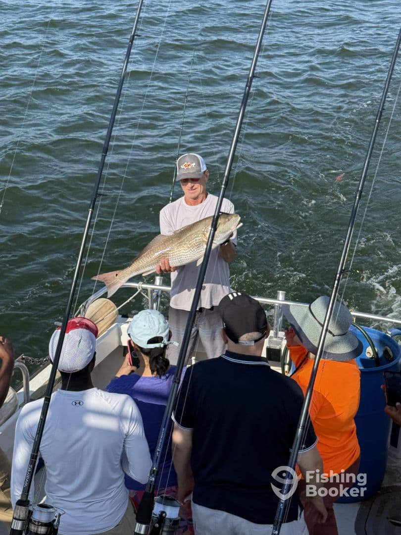 A proud angler displaying a large Redfish on a charter boat, surrounded by fellow fishing enthusiasts.