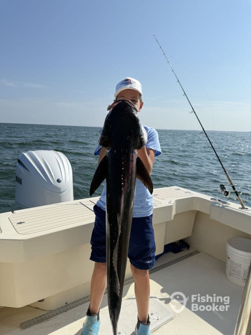 A young angler proudly displaying a large Cobia on a fishing boat, showcasing a successful day on the water.