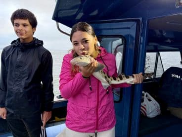 Young angler proudly holding a Spotted Catshark aboard a fishing boat, showcasing a successful catch during a family fishing trip.