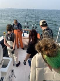 A group of young anglers engaged in fishing activities aboard a boat, with multiple fishing rods set up in the background.