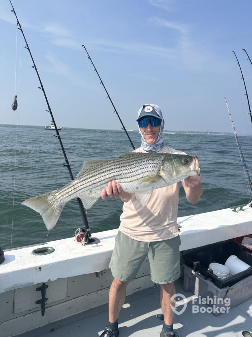 An angler proudly displaying a large Striped Bass while fishing on a boat, showcasing a successful day on the water.