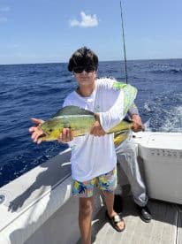 A young angler proudly displaying a vibrant Mahi Mahi while fishing offshore, showcasing a sunny day on the water.