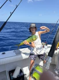 A young angler proudly displaying a vibrant Mahi Mahi while fishing offshore, showcasing a sunny day on the water.