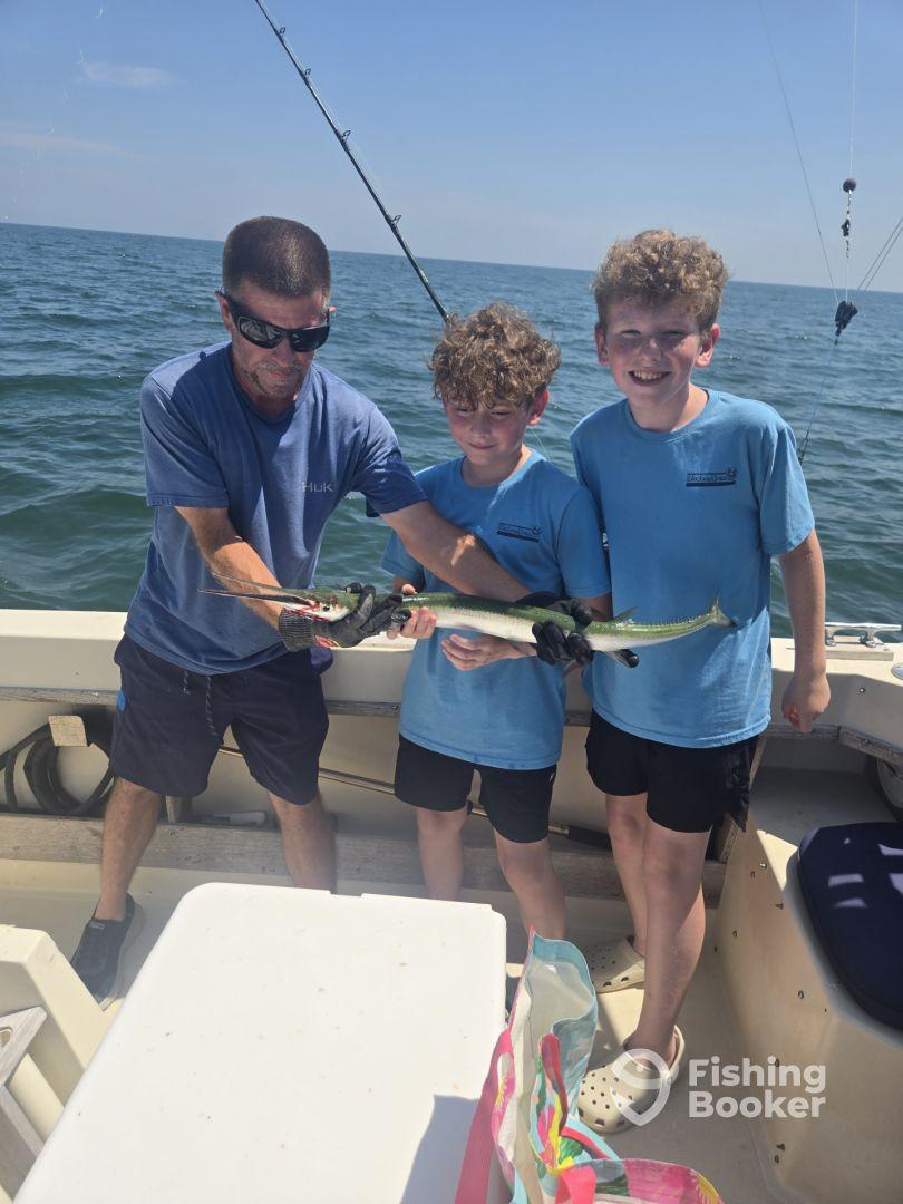 Two young anglers proudly displaying a large Barracuda while fishing on a boat in open waters.