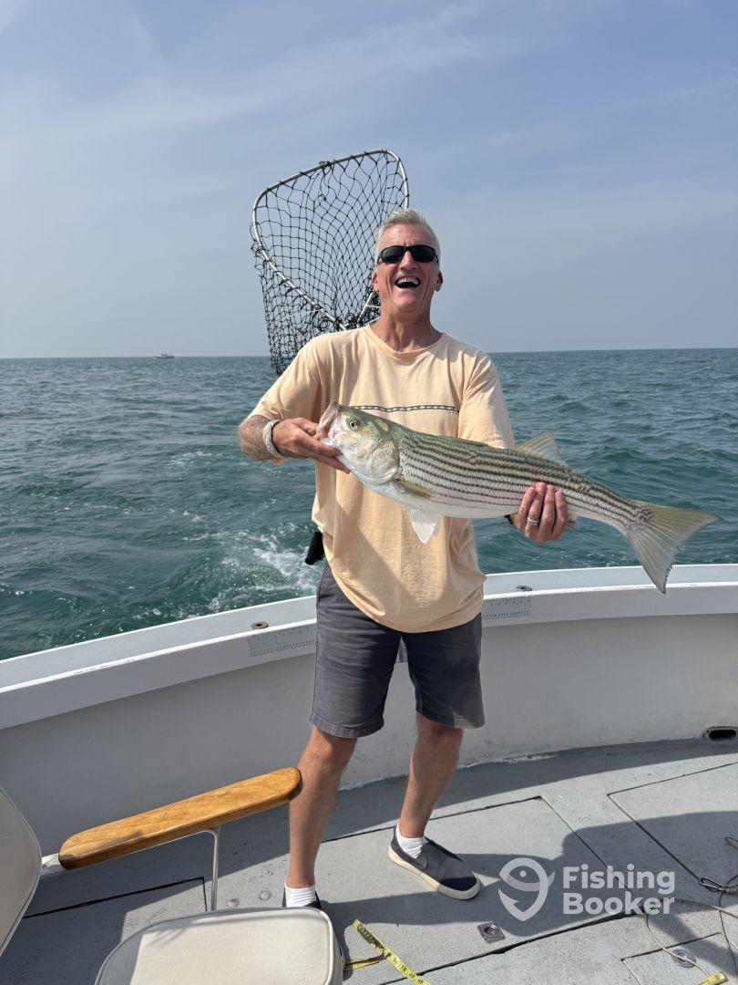 An enthusiastic angler proudly displaying a large Striped Bass while fishing on a boat in open waters.