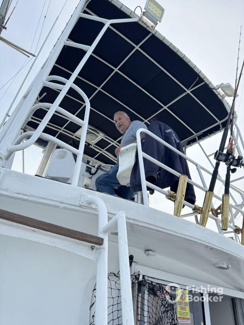 A smiling captain at the helm of a spacious fishing boat, showcasing the interior layout and seating area.