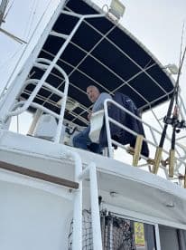 A smiling captain at the helm of a spacious fishing boat, showcasing the interior layout and seating area.