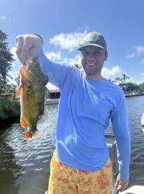 Angler proudly displaying a vibrant Largemouth Bass while fishing from a boat in a scenic waterway.