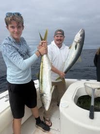 Two anglers proudly displaying their catch of Yellowtail Snapper while fishing offshore, showcasing a successful day on the water.