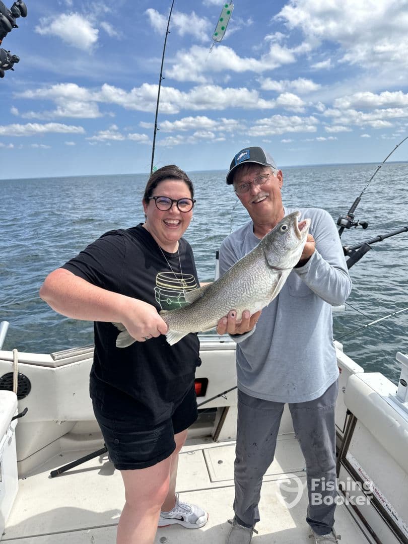 Two anglers proudly displaying a large Lake Trout on a fishing boat, enjoying a sunny day on the water.