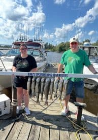 Two anglers proudly displaying their catch of multiple trout on a board at the dock, showcasing a successful fishing trip with King's Sportfishing Adventures.