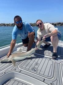 Two anglers proudly displaying a caught shark on the deck of a boat during a sunny fishing trip.