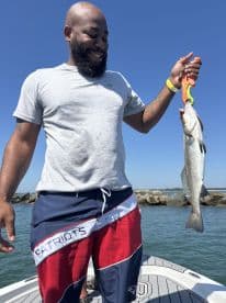 An angler proudly displaying a large striped bass while standing on a boat, enjoying a sunny day on the water.