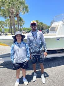 A young boy and a fishing guide pose together in front of a boat at a sunny dock, showcasing a family-friendly fishing environment.