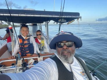 A family enjoying a fishing trip on a boat, with two children wearing life jackets and smiling for the camera.