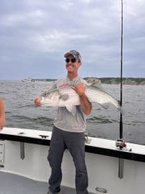 An angler proudly displaying a large striped bass while fishing offshore, showcasing a successful day on the water.