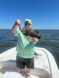 An angler proudly displaying a large Grouper while fishing on a sunny day in open waters.
