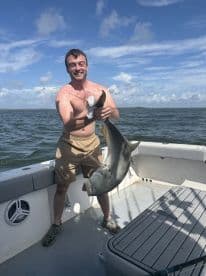 Angler proudly displaying a large fish while aboard a fishing boat in a sunny coastal environment.
