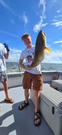 A young angler proudly displaying a large fish aboard a fishing charter, enjoying a sunny day on the water.