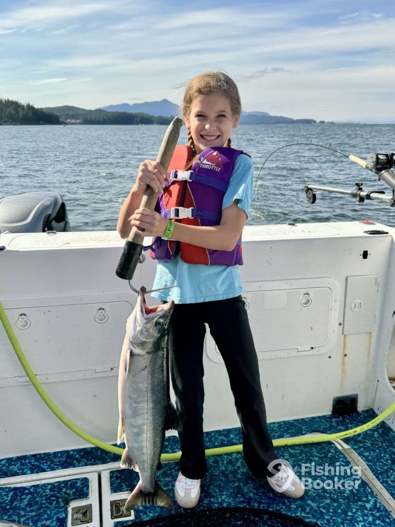 Young angler proudly holding a large salmon on a boat, showcasing a successful fishing trip in a scenic waterway.