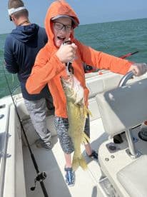 A young angler proudly displaying a Walleye while fishing on a boat, showcasing a fun day on the water.