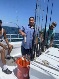 A young angler proudly displaying a caught fish aboard a fishing charter, surrounded by fellow anglers and fishing gear.