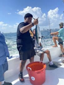 A young angler proudly displaying a caught fish on a fishing charter in sunny waters, with fellow anglers enjoying the day on the boat.