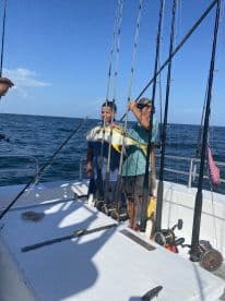 A young angler and an adult proudly displaying a large fish on a fishing charter in open waters, surrounded by fishing rods.